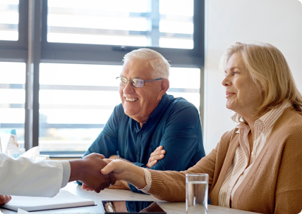 Smiling doctor shakes hands with senior couple across a table